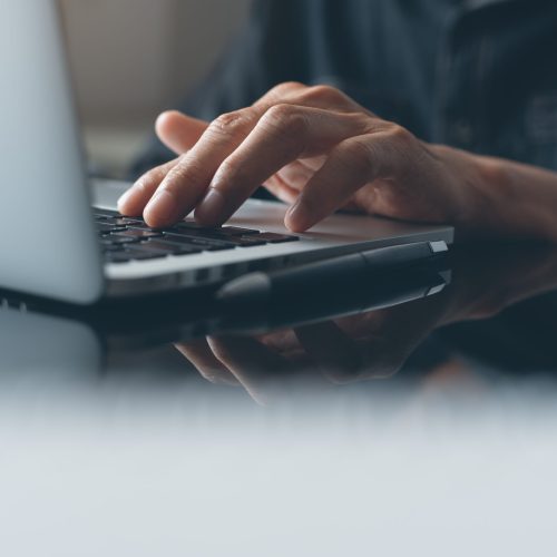 Casual business man, hipster hand typing on keyboard, working on laptop computer on desk in modern office or home office, online working concept, close up